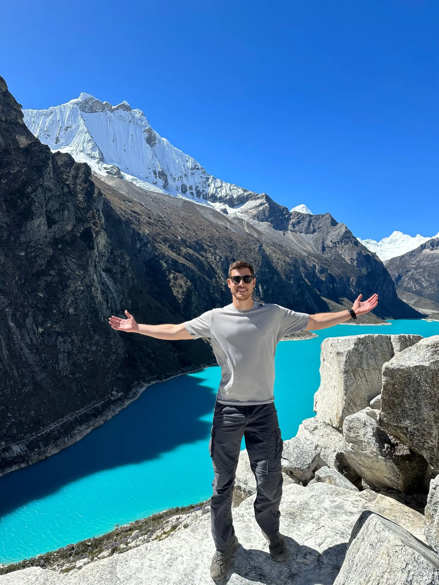 Ben standing on a rock above a turquoise mountain lake, his arms stretched wide