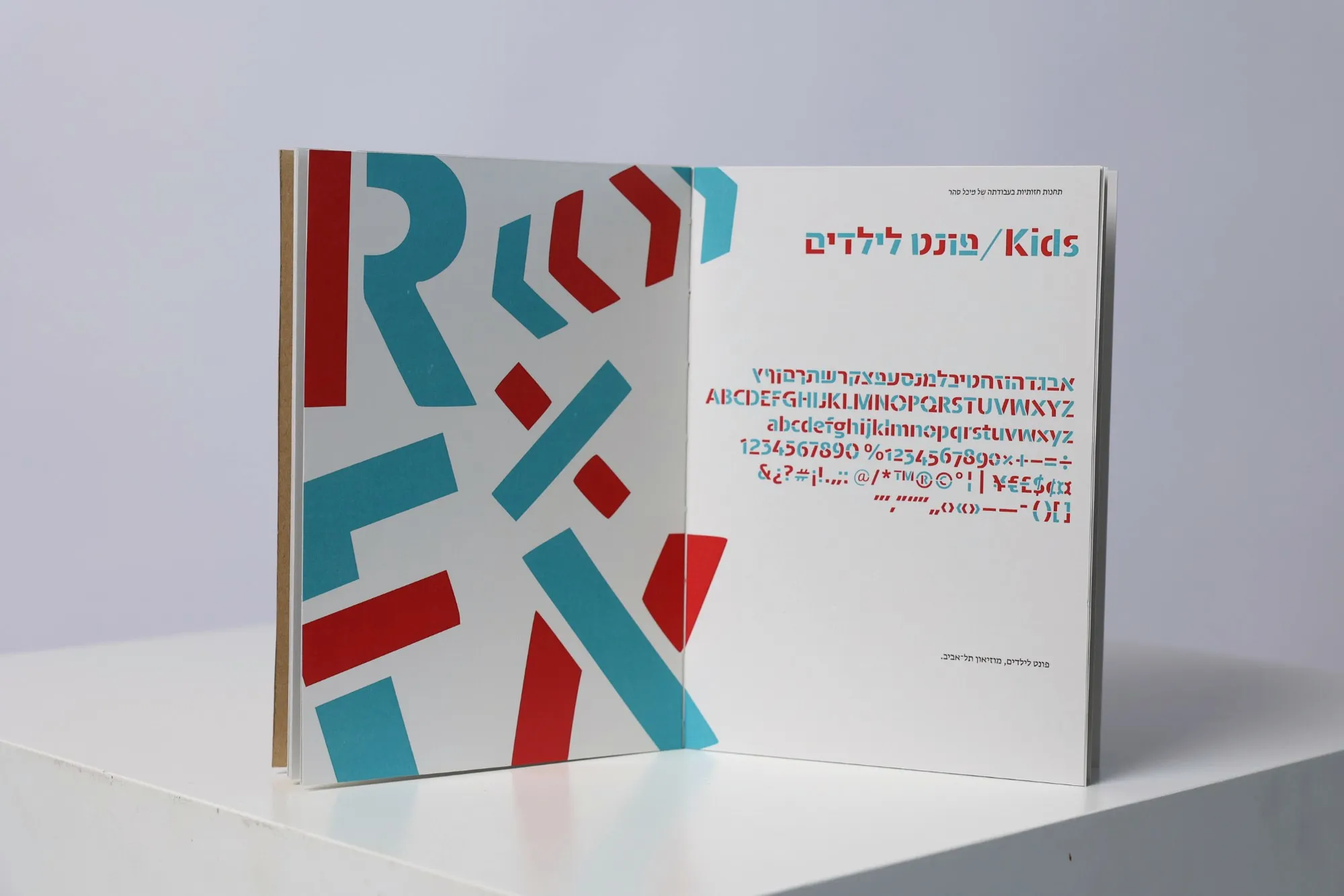 A spread for a children's typeface, its letters cut into red and blue shapes on the left page and the full character set on the right