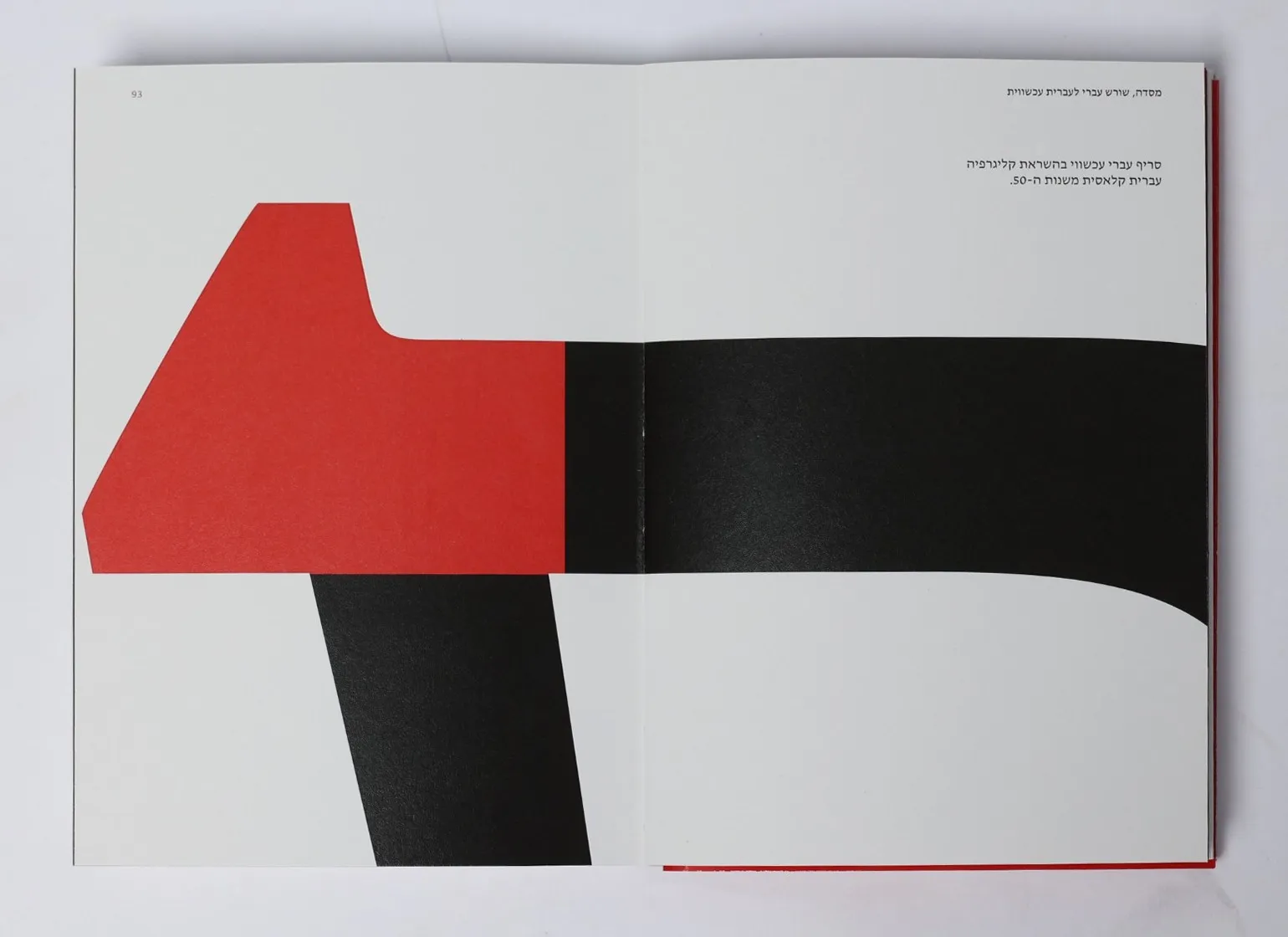 The catalogue open flat at a spread from the Masada chapter: one letter drawn across both pages in black, its serif in red, and a short Hebrew line at the top right