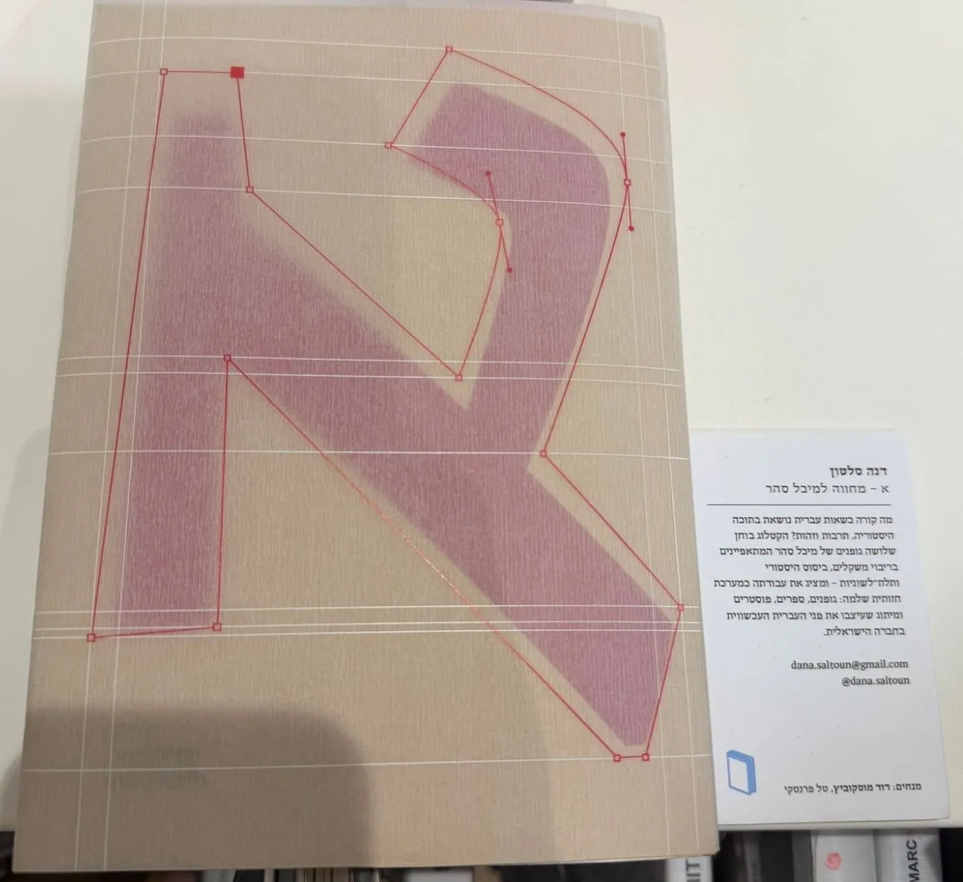 The catalogue on the exhibition table seen from above, its jacket over the kraft cover, beside a card with Dana's name and a short text