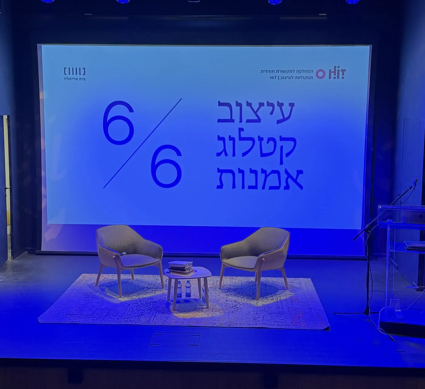 The stage at Beit Ariela before the closing event, two armchairs under a screen reading 6/6 Art Catalog Design