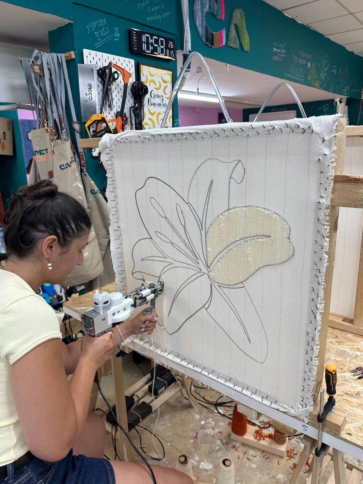 Dana working a tufting gun across a stretched canvas with a flower drawn on it